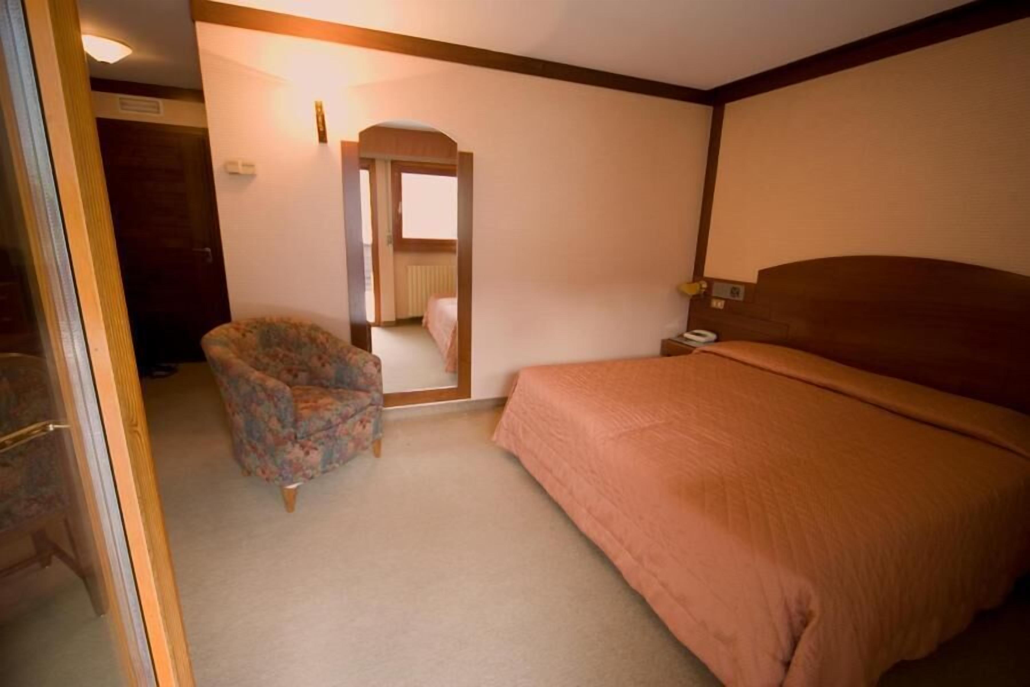 A bedroom with a bed, a chair, and a door leading to another room.