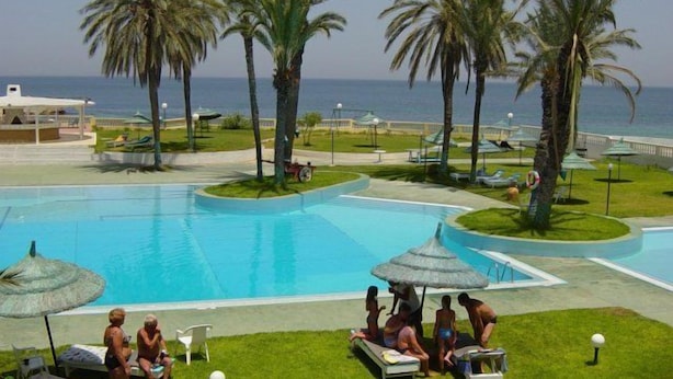 Un área de piscina con palmeras, sillas de descanso y sombrillas.