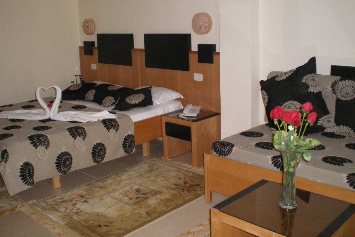 Habitación de hotel con dos camas, una mesita, un florero con flores y un teléfono en la mesita de noche.
