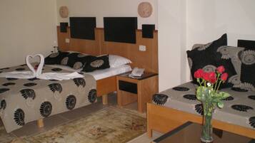 A hotel room with two beds, a small table, a vase with flowers, and a telephone on the nightstand.