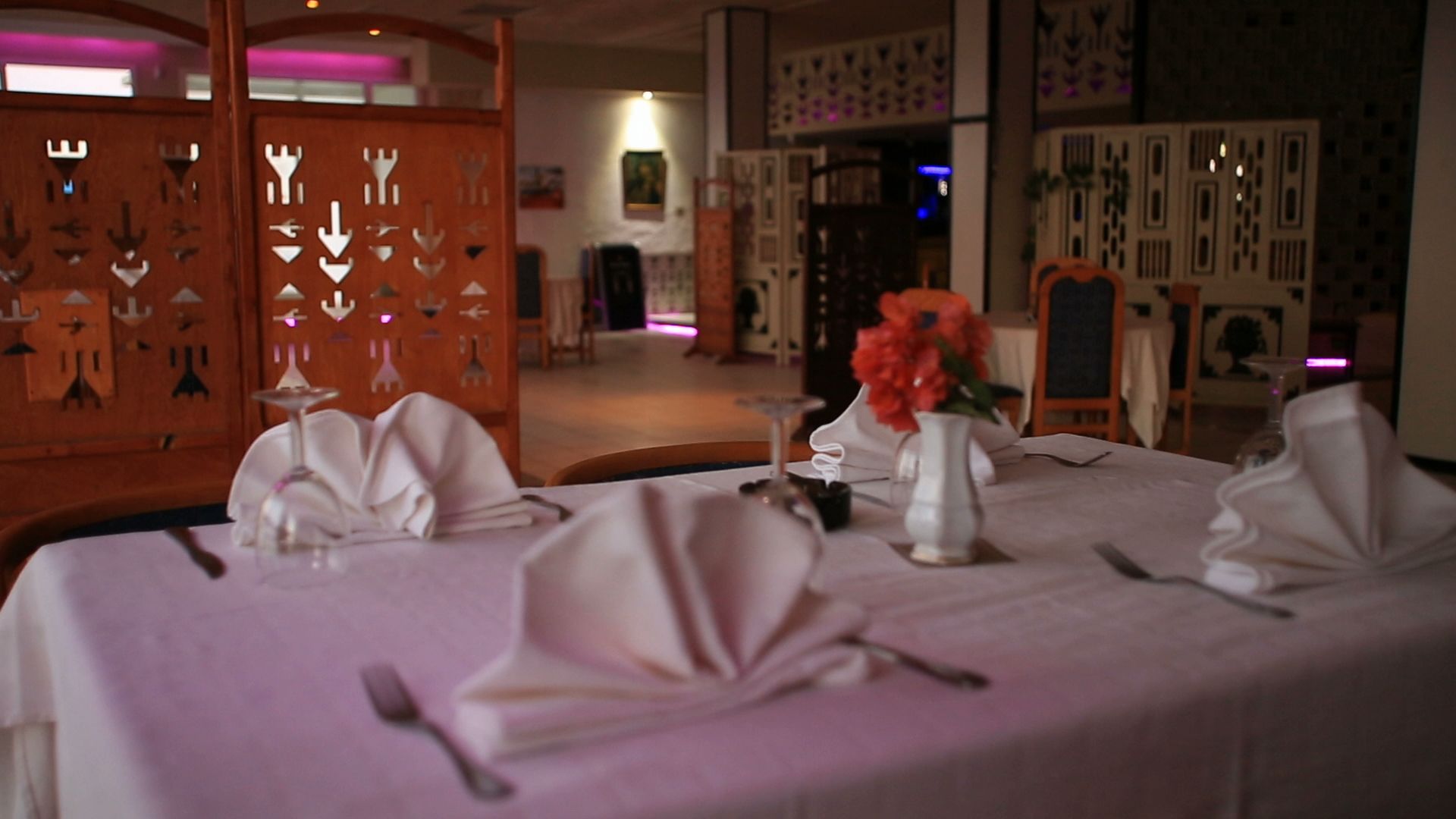 A dining area with tables set for a meal, featuring white tablecloths and silverware.