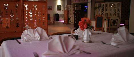 A dining area with tables set for a meal, featuring white tablecloths and silverware.