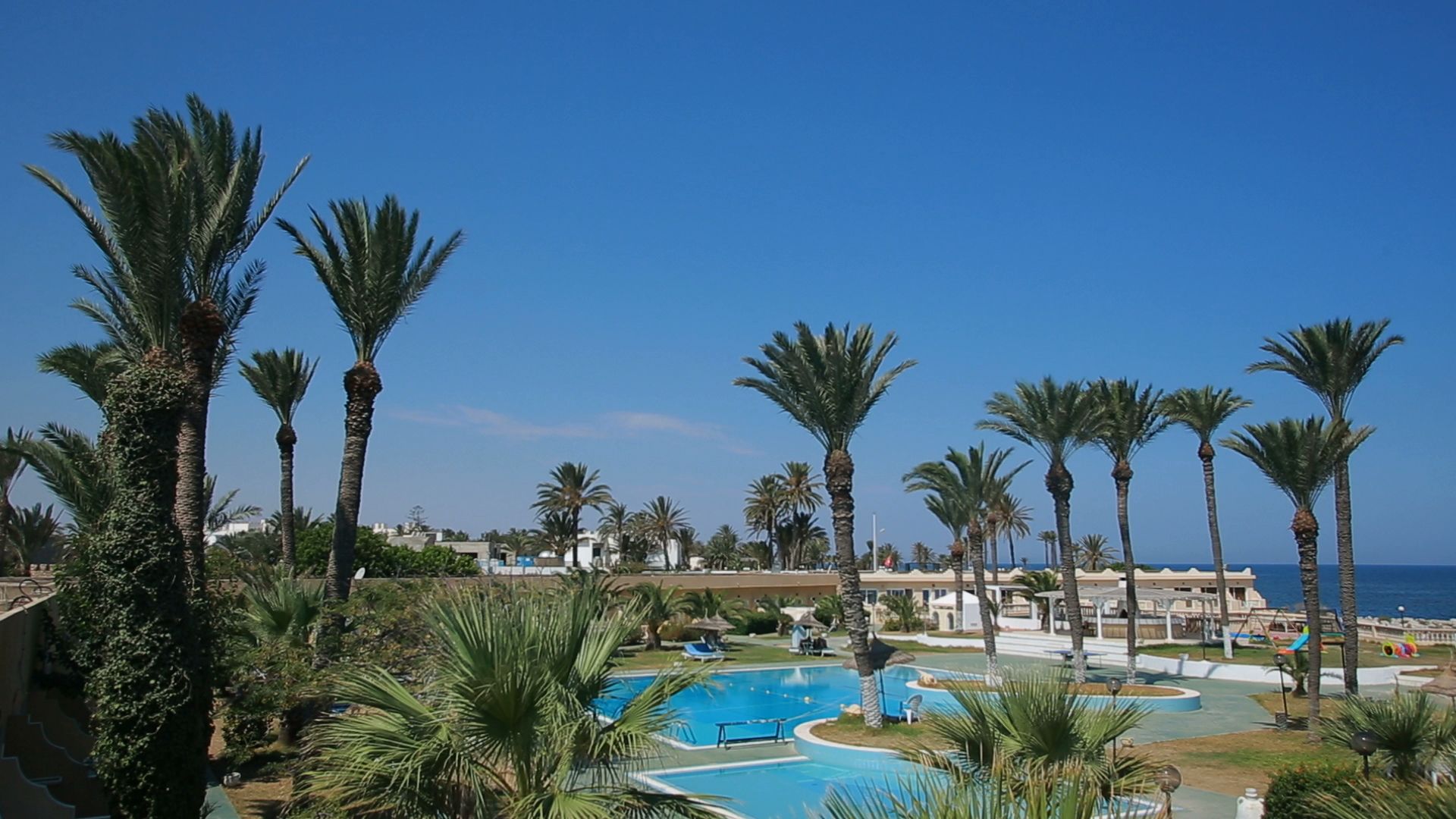 A resort with multiple swimming pools, palm trees, and a clear view of the ocean.