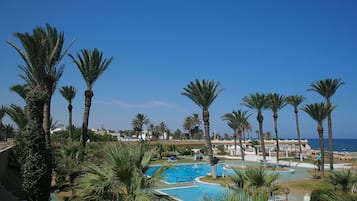 A resort with multiple swimming pools, palm trees, and a clear view of the ocean.