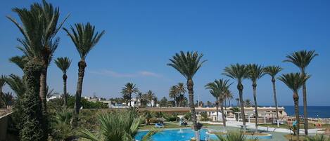 A resort with multiple swimming pools, palm trees, and a clear view of the ocean.