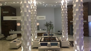 Un vestíbulo moderno con pilares blancos y geométricos, una recepción y asientos contemporáneos.
