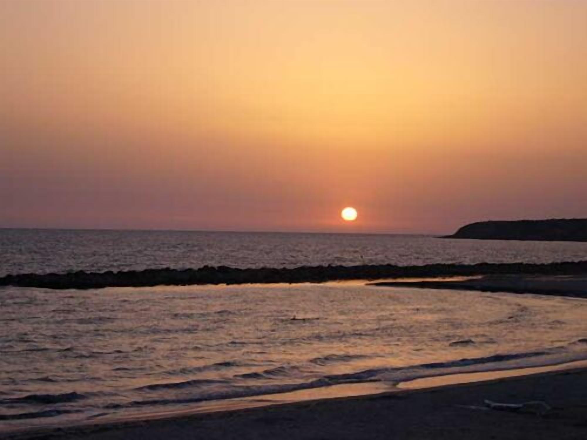 A sunset over a beach with waves gently lapping at the shore.