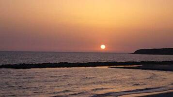 A sunset over a beach with waves gently lapping at the shore.
