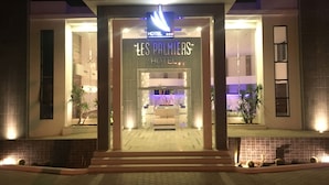 La entrada del Hotel Les Palmiers, con un diseño moderno, que presenta un fachada de vidrio y una entrada acogedora.