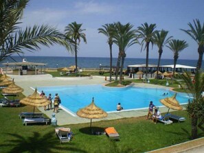 Un espace piscine agrémenté de chaises longues et de parasols, entouré de palmiers et offrant une vue sur la mer.