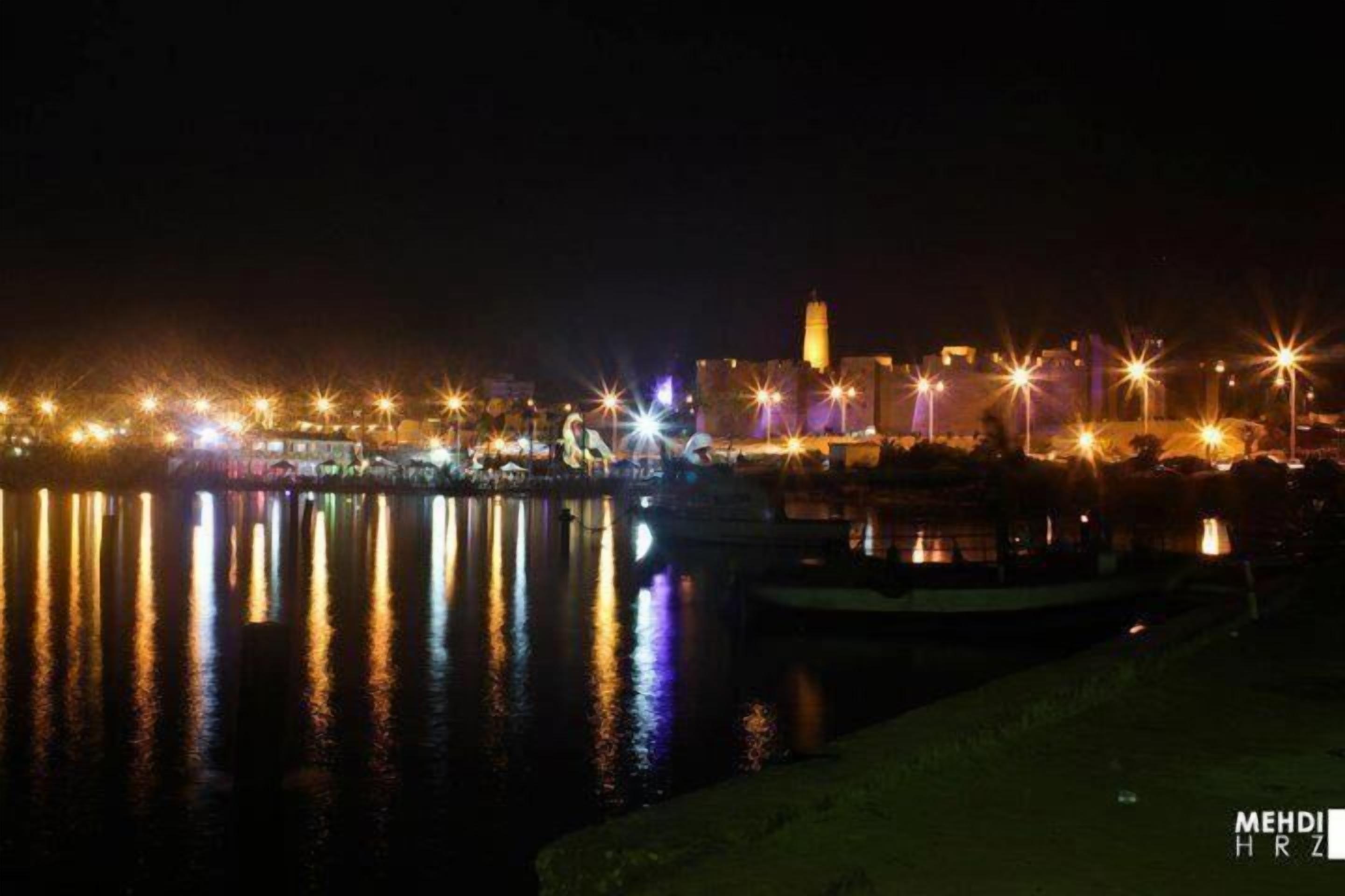 A nighttime view of a waterfront cityscape with illuminated buildings and a prominent tower.