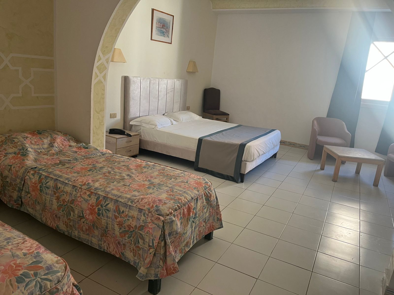 Una habitación de hotel con cama, una silla, una mesita pequeña y una mesita de noche.