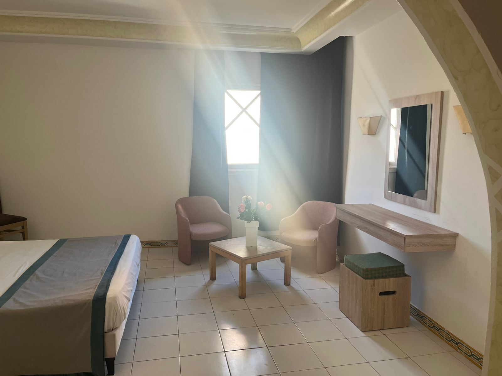 Ein Hotelzimmer mit Bett, zwei Sesseln, einem kleinen Tisch, einem Spiegel und einem Fenster mit Vorhängen.
