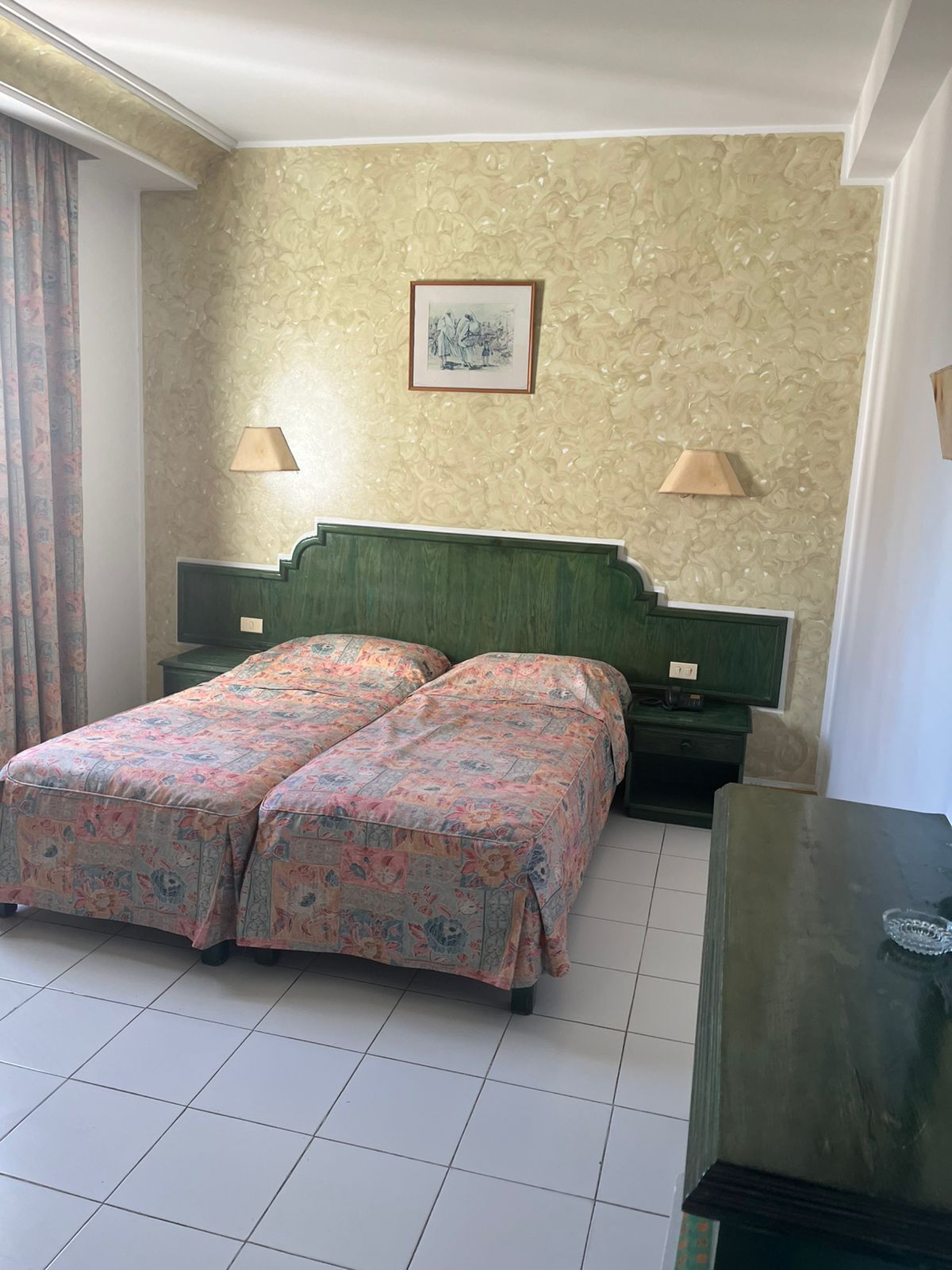 Un letto matrimoniale con biancheria da letto floreale, due comodini con lampade, un quadro appeso alla parete e una testiera verde.