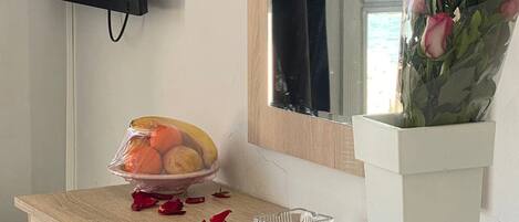 Escritorio de madera con un frutero, un cenicero de vidrio y un florero. Un televisor está montado en la pared sobre el escritorio.