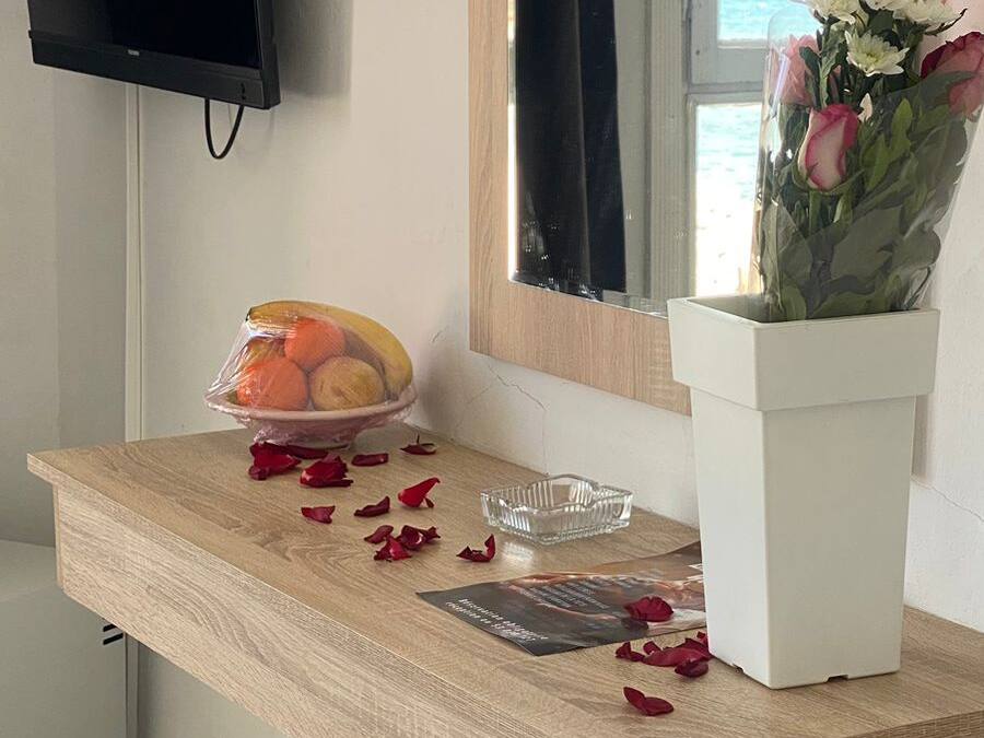 Een houten bureau met een schaal fruit, een asbak van glas en een bloemenvaas. Een televisie is aan de muur boven het bureau bevestigd.