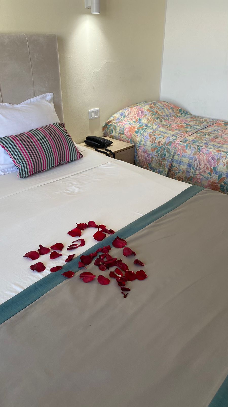 A hotel room with a bed, a bedside phone, and a floral-patterned bedspread.