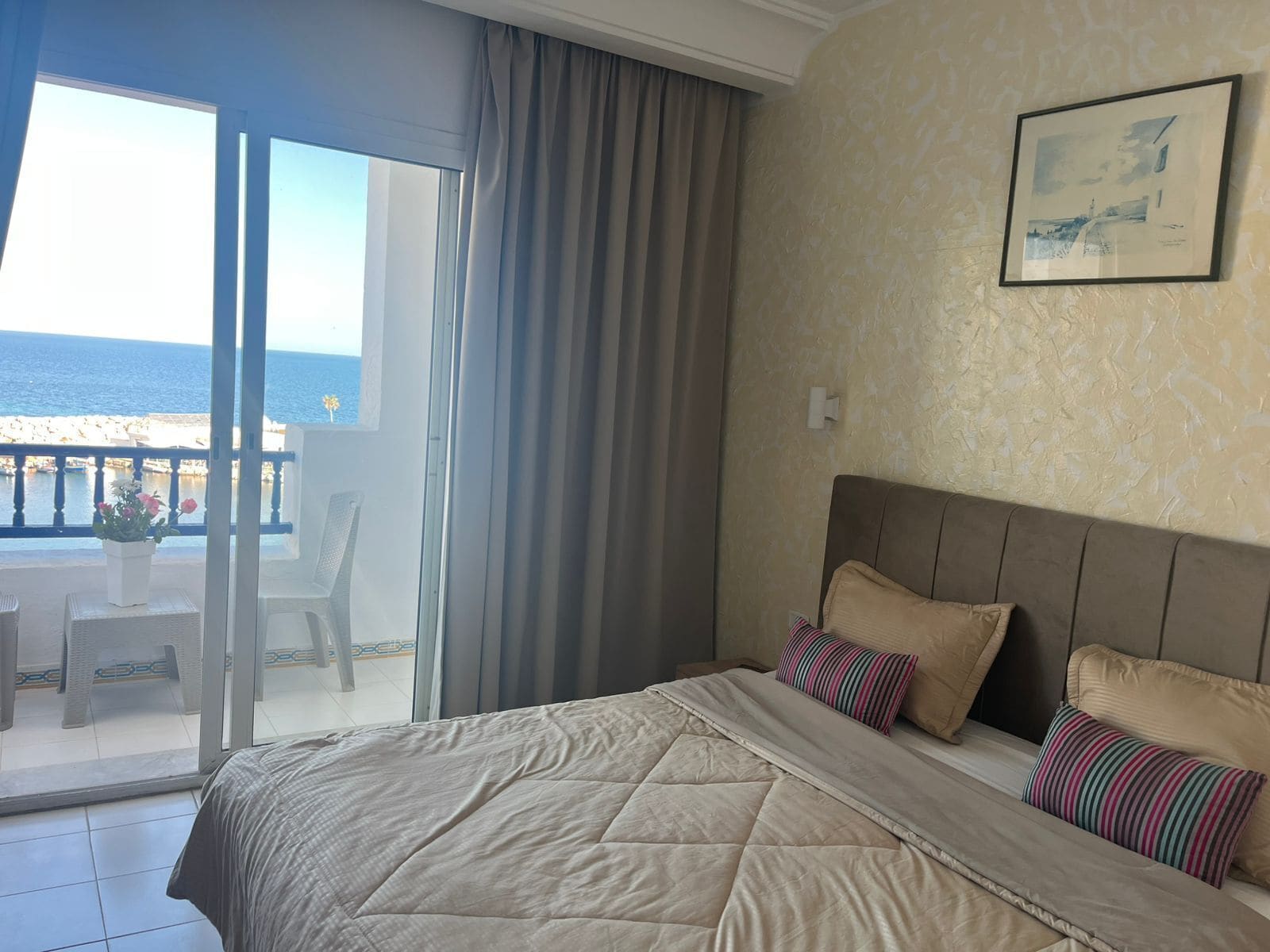 A bedroom with a large bed, a view of the sea through a sliding glass door, and a framed picture on the wall.