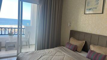 A bedroom with a large bed, a view of the sea through a sliding glass door, and a framed picture on the wall.