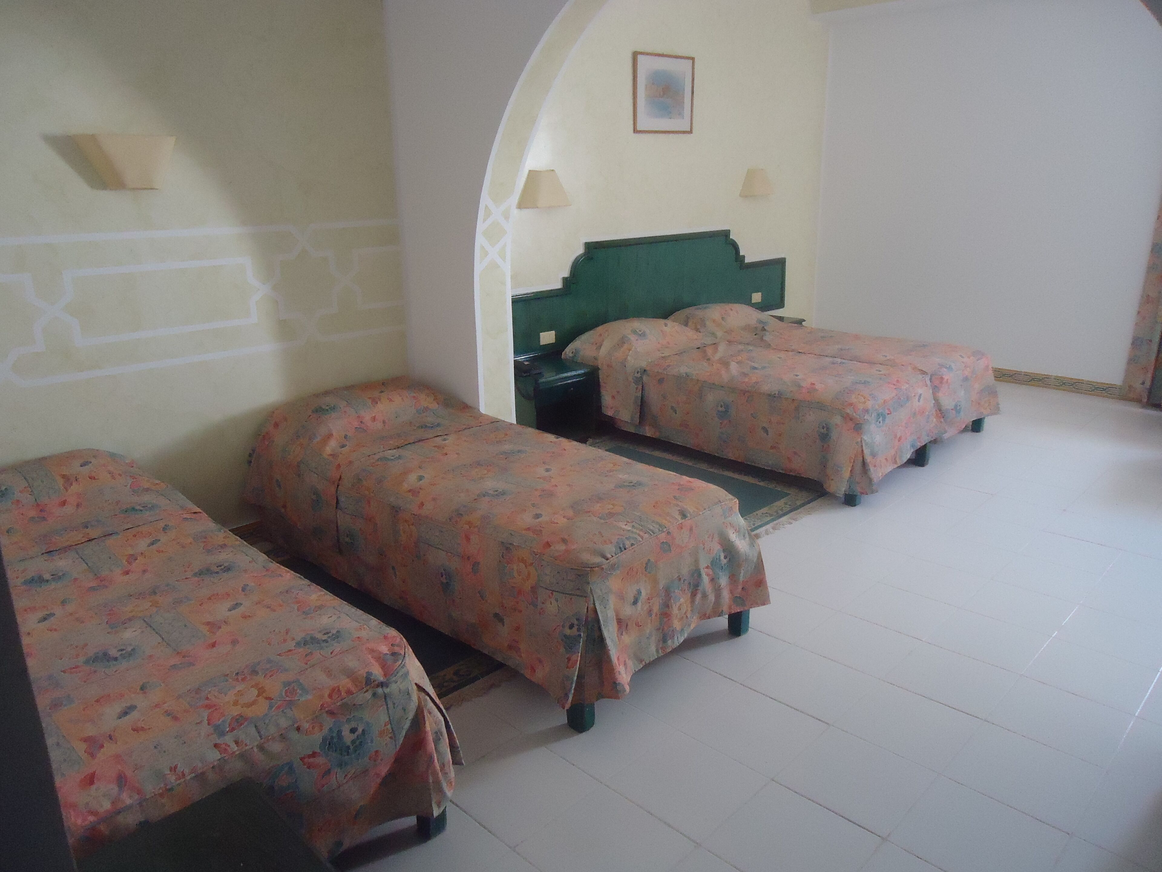 A room with three single beds, a green headboard, two wall lamps, and a framed picture on the wall.