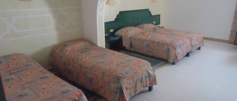 A room with three single beds, a green headboard, two wall lamps, and a framed picture on the wall.