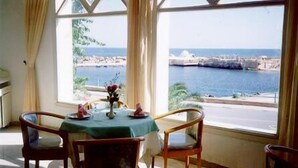 Un comedor con una mesa preparada para dos personas, un jarrón de flores y vista al mar y la costa rocosa a través de amplias ventanas.