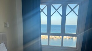 Una habitación de hotel con una cama, un ventanal con vistas al mar y una cortina.