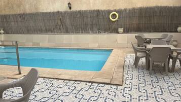 Piscina com deck revestido, rodeada por cadeiras e mesas de vime.