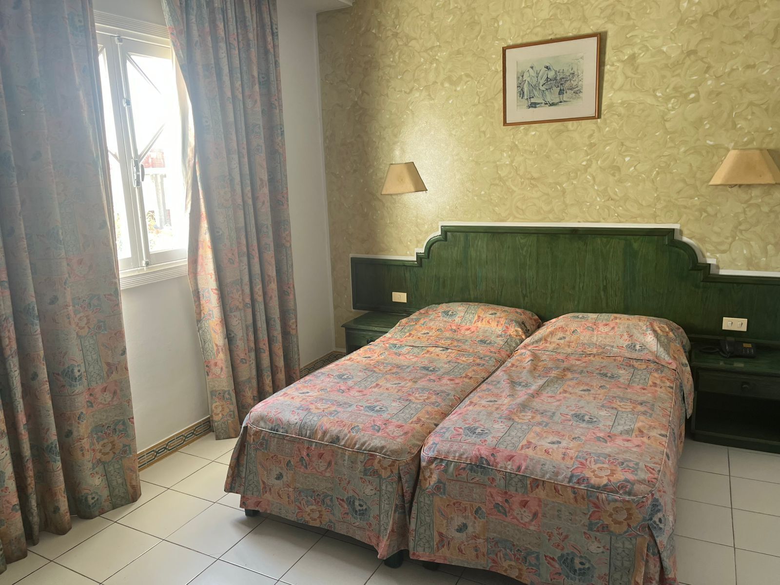 Un letto matrimoniale con biancheria da letto floreale, due lampade ai comodini, un quadro appeso alla parete e una finestra con tende.
