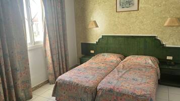 Un letto matrimoniale con biancheria da letto floreale, due lampade ai comodini, un quadro appeso alla parete e una finestra con tende.