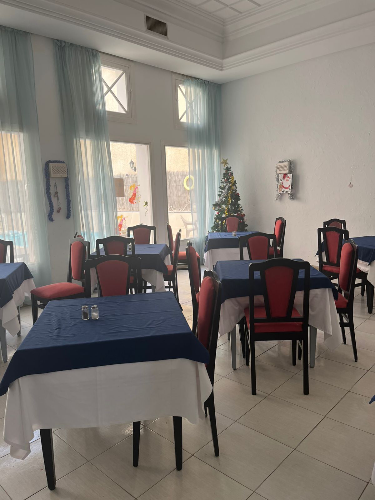 A dining area with tables and chairs, a Christmas tree, and a view of the outside.