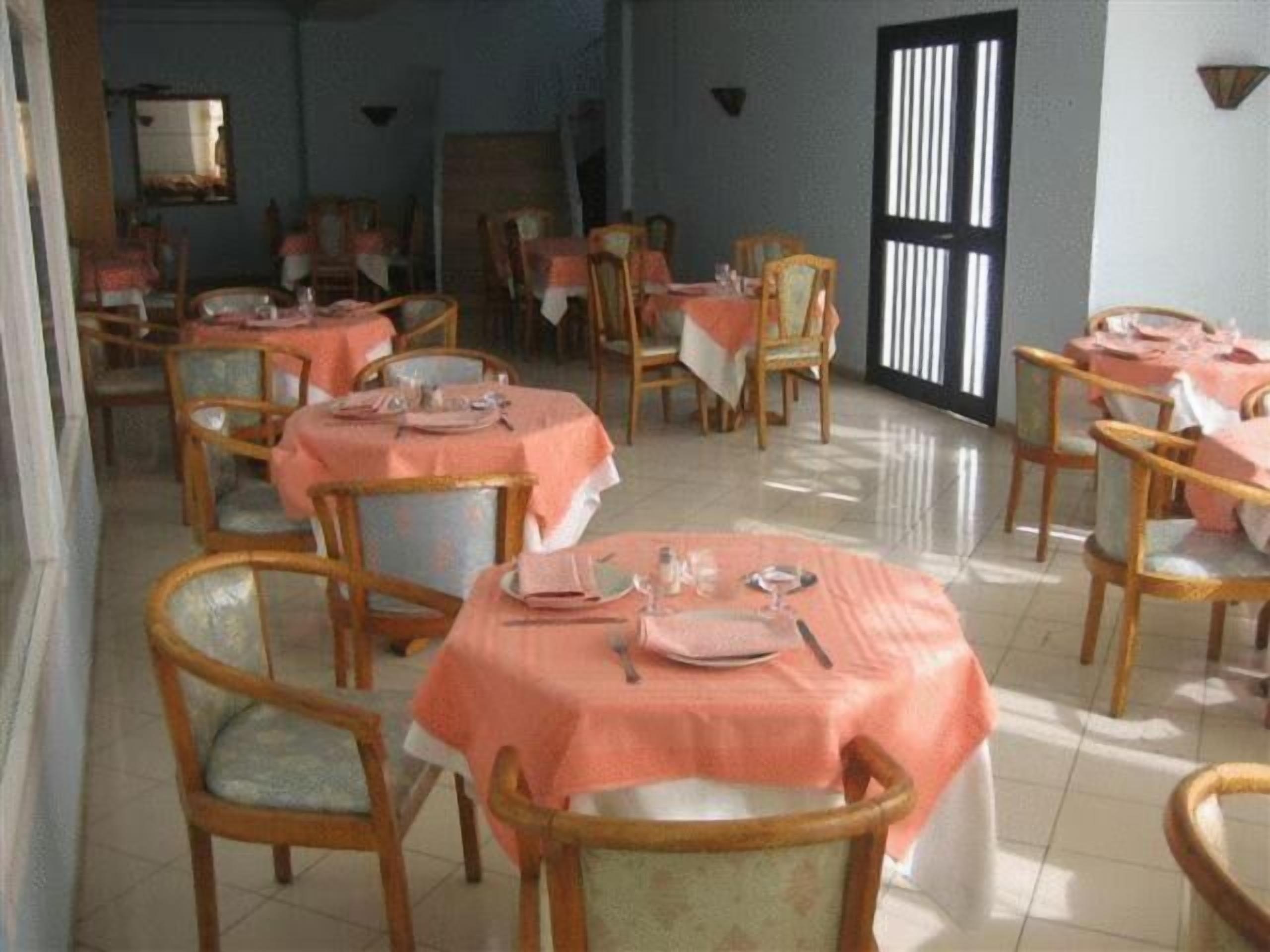 Un comedor con mesas redondas cubiertas con manteles rosas, sillas de madera y piso de baldosas.
