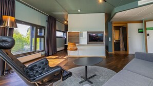 Une chambre d’hôtel moderne avec un fauteuil inclinable en cuir, un canapé gris, une petite table ronde et un téléviseur.