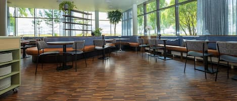 A spacious indoor seating area with wooden flooring, large windows, and a variety of seating options including benches and chairs.