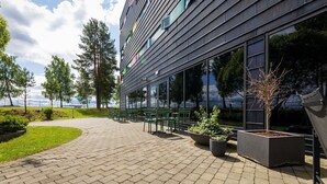 Un bâtiment moderne doté de grandes fenêtres, d’une terrasse et d’un chemin piétonnier dallé.