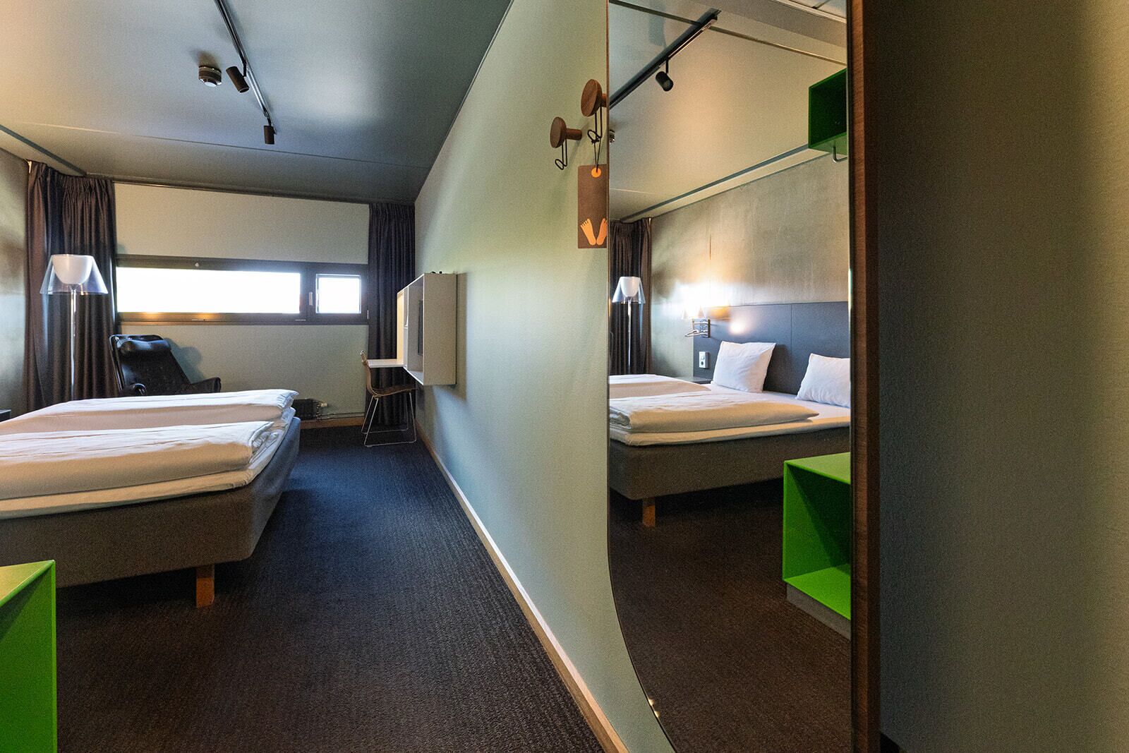 A hotel room with two beds, a desk, a chair, and a mirror.