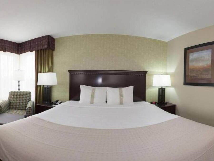 A hotel room with a large bed, a chair, a desk, and a lamp.