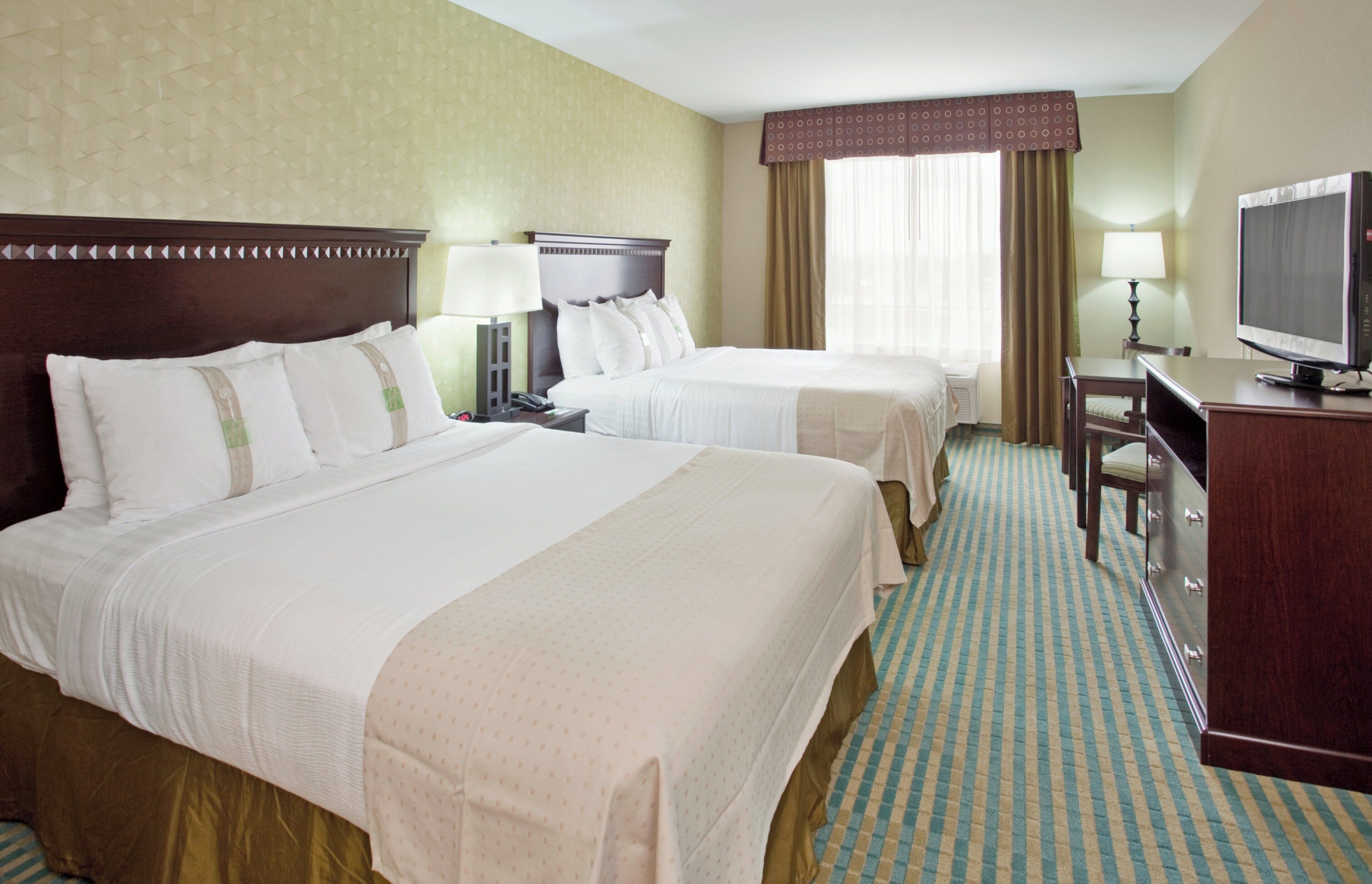 A hotel room with two beds, a desk with a television, and a window with curtains.