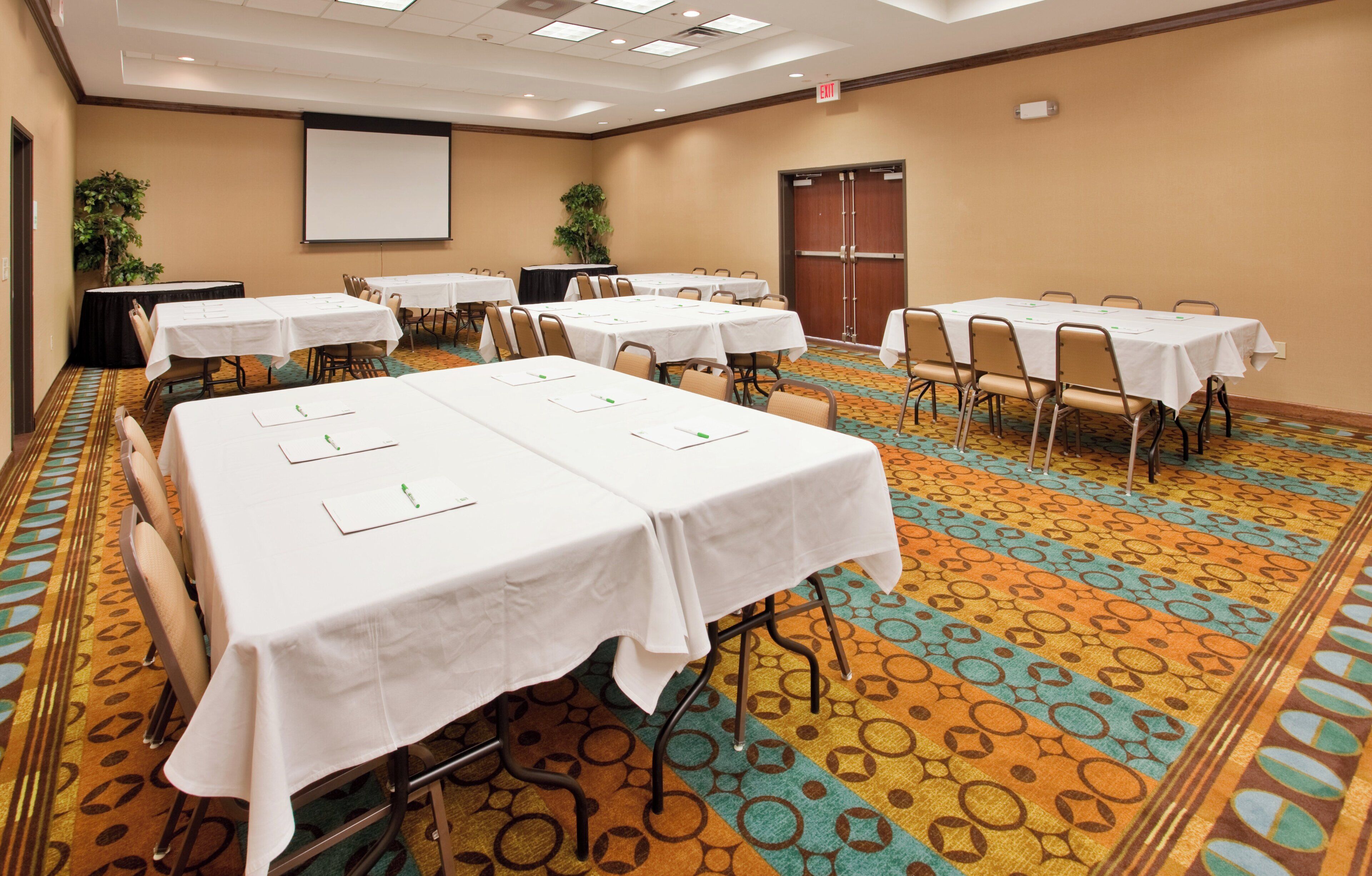 A conference room with multiple tables, chairs, and a projector screen.