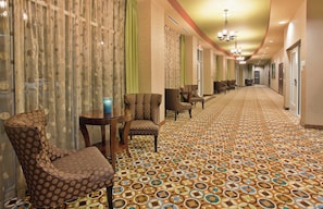 A hotel corridor with patterned carpet, seating area with chairs and a table, and a chandelier. - Holiday Inn Columbia East by IHG (Columbia)