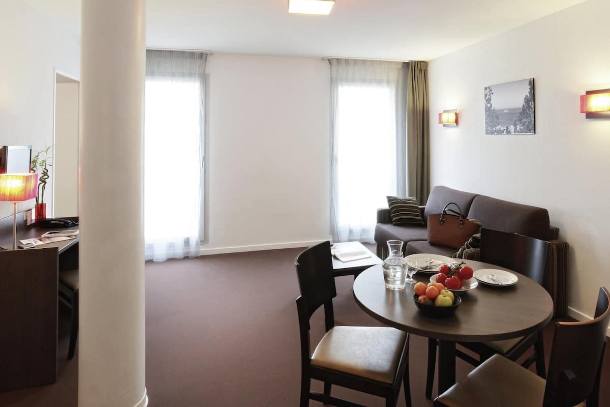 Une chambre d’hôtel avec une table à manger dressée pour deux personnes, un canapé et une lampe.