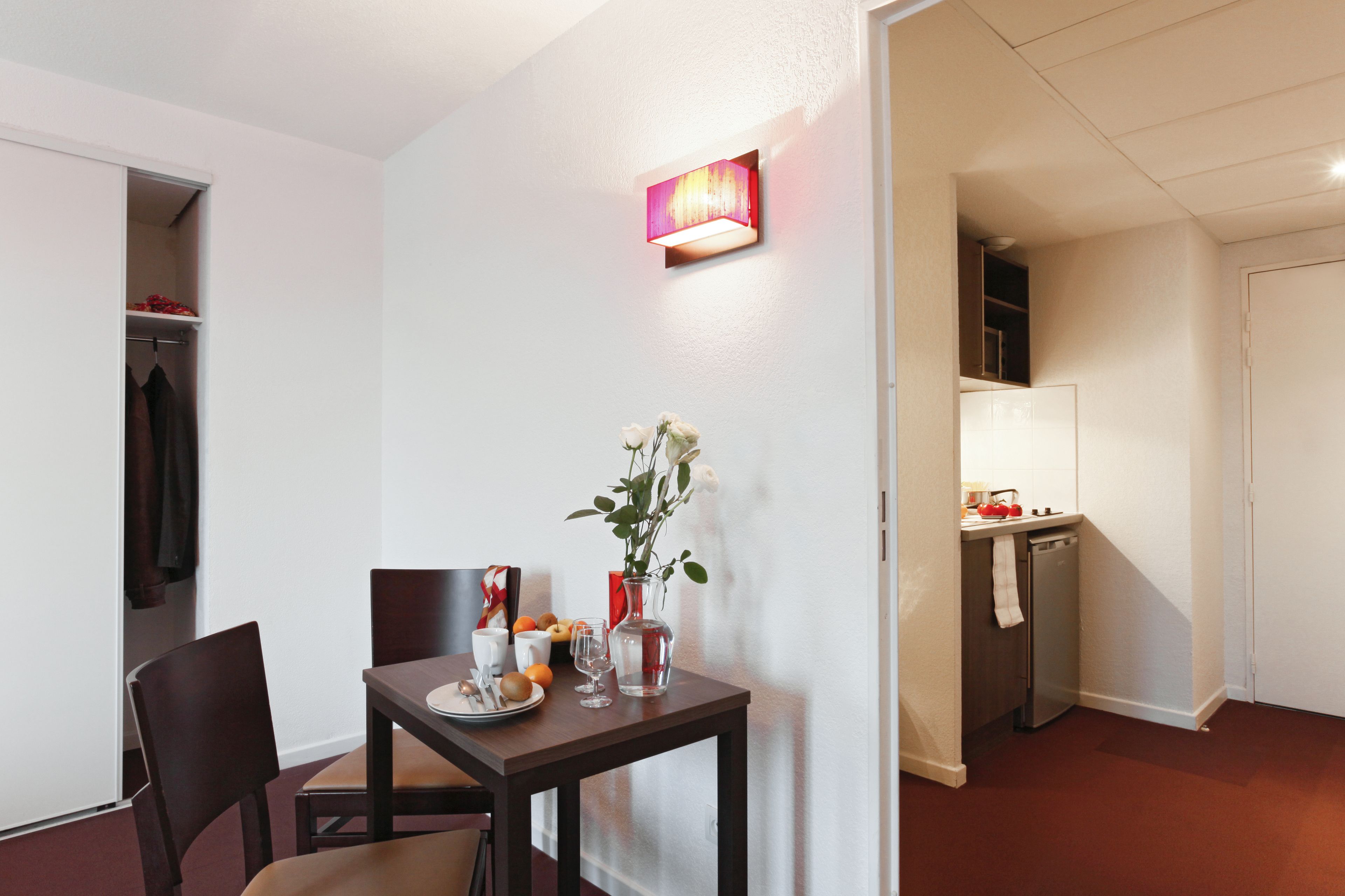 A compact dining area with a table set for two, a vase with flowers, and a wall-mounted light fixture.