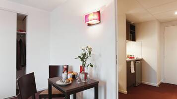 A compact dining area with a table set for two, a vase with flowers, and a wall-mounted light fixture.