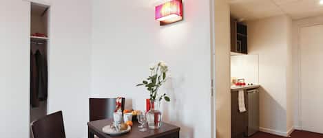 A compact dining area with a table set for two, a vase with flowers, and a wall-mounted light fixture.