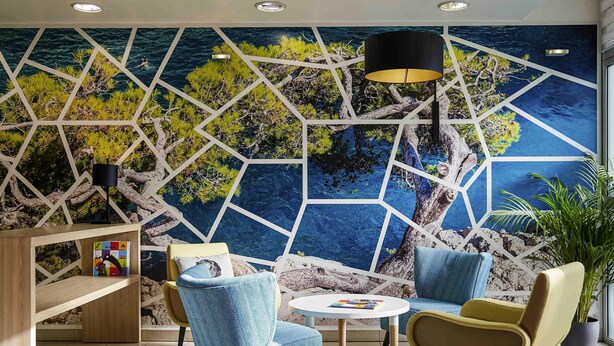 Ein moderner Lounge-Bereich mit einer geometrischen Wandmalerei, einem runden Tisch und zeitgemäßen Sesseln.