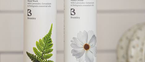 Dos botellas de jabón de manos y crema hidratante con aceites esenciales de lavanda, geranio y petitgrain de Bramley sobre una encimera blanca.
