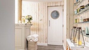 A bathroom with wooden paneling, a round door, a shelf with toiletries, and a wicker basket with towels. - Harbour Hotel Chichester (Chichester)