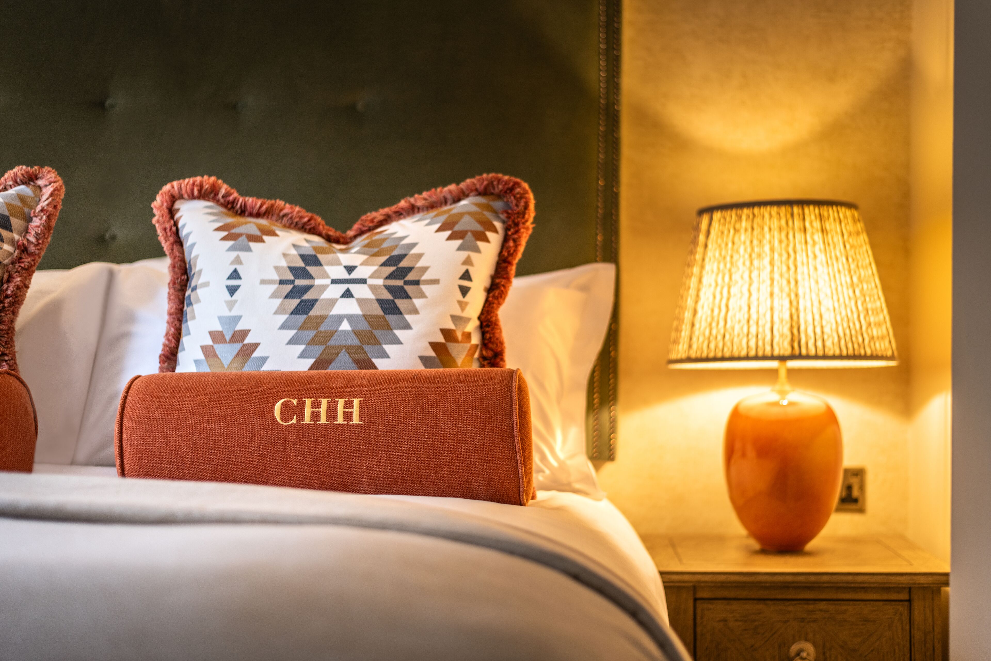 A neatly made bed with patterned pillows and a red accent pillow with "CHH" embroidered on it.