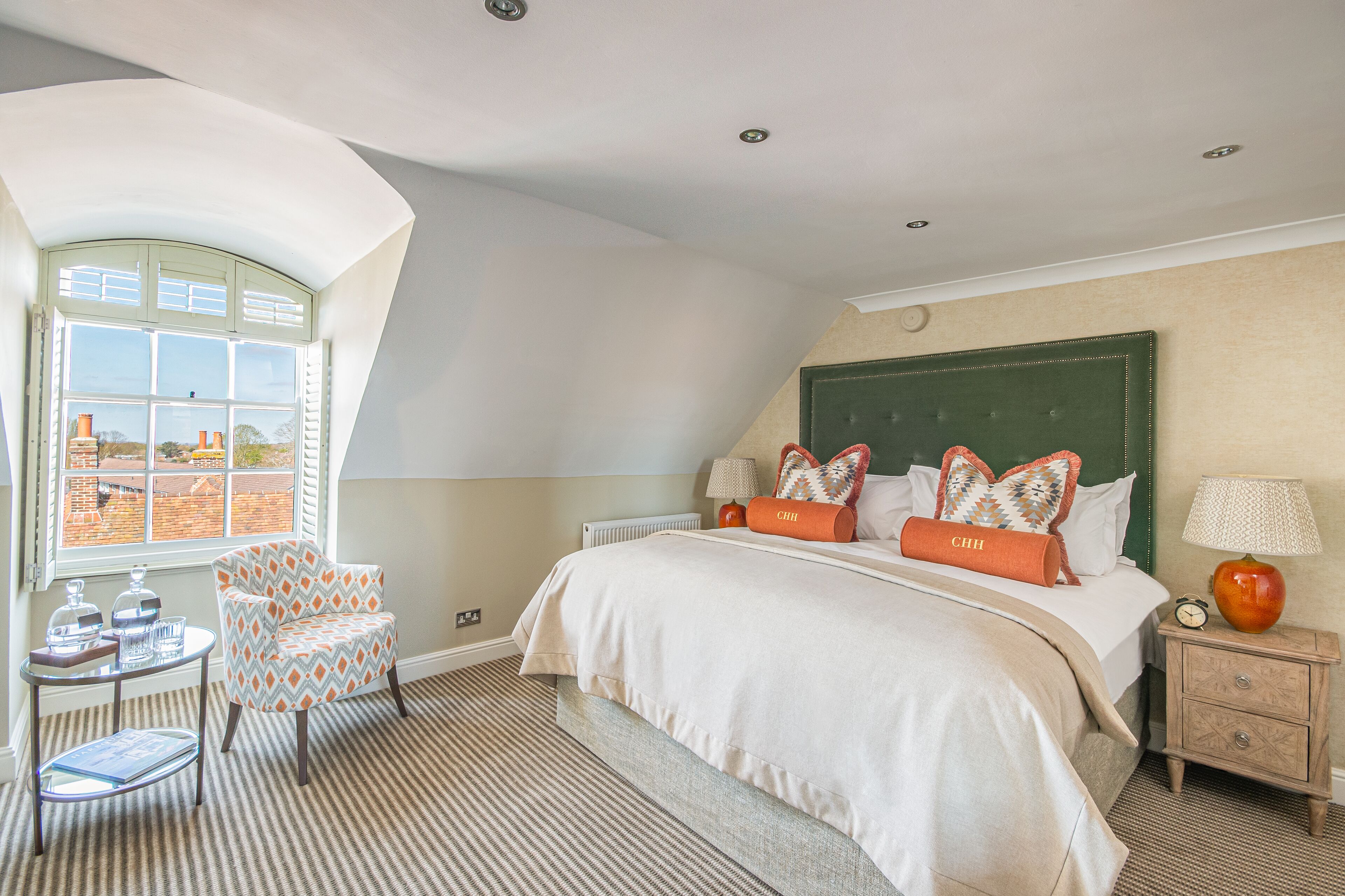 A bedroom with a large bed, a chair, a bedside table, a lamp, and a view of the outside.