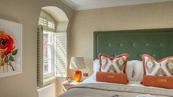 A neatly made bed with a green headboard, two pillows with 'CHH' embroidered, a lamp, a framed picture, and a magazine on the bed.